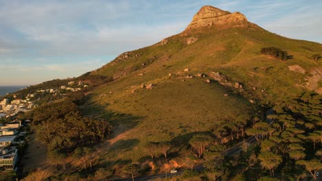 Car-driving-towards-Pipe-Track-and-Lions-Head-in-background-at-sunset-in-Cape-Town,-aerial