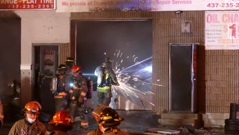 Firefighter-Crew-Using-Circular-Saw-Cutting-through-Garage-Doors-of-'Danforth-and-Warden'-Auto-Body-Repair-Shop-in-Scarborough,-Toronto