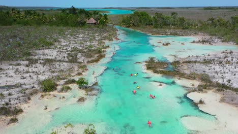 tourists-floating-down-the-tropical-blue-Los-Rapidos-in-Bacalar-Mexico-on-sunny-day,-aerial