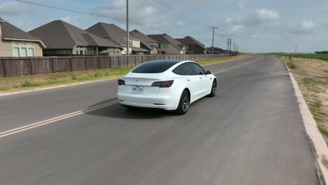 Aerial-tracking-of-rear-and-side-of-white-Tesla-Model-3-driving-in-rural-Texas-community