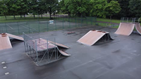 Aerial-view-flying-low-across-fenced-skate-park-ramp-in-empty-closed-playground