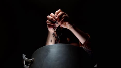hands-of-a-cook-pouring-beans-in-a-large-metal-pot-in-spot-light-with-a-dark-background