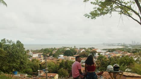 Couple-watching-city-landscape-full-of-old-houses,-trees,-ocean-and-buildings-on-the-horizon-on-a-cloud-day