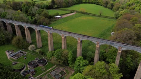 Aerial-view-following-narrow-boat-on-Trevor-basin-Pontcysyllte-aqueduct-crossing-in-Welsh-valley-countryside-birds-eye-pull-away