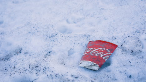 Close-slow-panning-shot-of-flat-paper-Coca-Cola-cup-in-snow-on-ground
