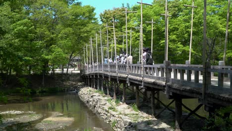 Menschen-Genießen-Die-Aussicht-Von-Der-Alten-Holzbrücke-Mit-Grünen-Bäumen-Im-Hintergrund-Im-Koreanischen-Volksdorf-In-Der-Stadt-Yongin,-Seoul,-Südkorea