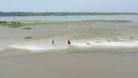 Drone-shot-of-Indian-romantic-couple-walking-on-beach-of-ganga-wearing-traditional-dress,-honeymoon-days
