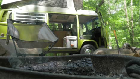 Volkswagen-Bus,-Wohnmobil,-Feuerring,-Schwelender-Campingstuhl,-Grüner-Wald,-Zeitlupe,-Handgehalten