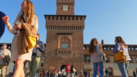 Low-angle-pov-of-tourists-walking-at-Sforza-Castle-in-Milan-with-clock-tower-in-background,-Italy