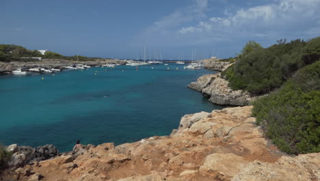 Scenic-view-of-tourists-swimming-in-clear-water-in-the-Cala-Santandria-creek-with-yachts-docked-on-the-shores