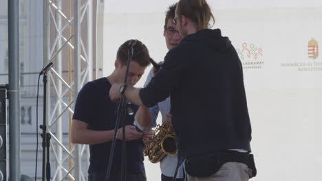 Band-crew-member-fixes-microphone-stand-for-saxophonist-performing-on-stage