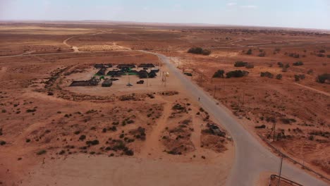 aerial-static-shot-of-army-camp-of-tents-in-the-middle-of-the-endless-desert-next-to-an-empty-road-with-single-soldier-walks-in-it