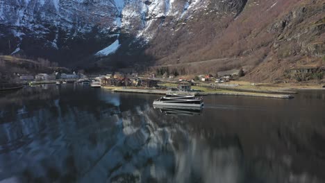 Aerial-following-passenger-catamaran-Vision-of-the-fjords-from-the-side-while-slowly-approaching-port-of-Flam---Beautiful-mountain-reflections-in-sea-and-Flam-in-background