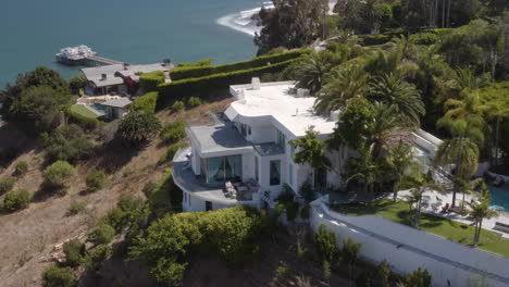 A-hillside-mansion-in-Malibu-California-with-the-Malibu-pier-and-Surfrider-Beach,-complete-with-surfers,-in-the-background