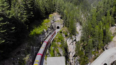 Aerial:-red-train-by-a-gorge-in-mountainous-landscape