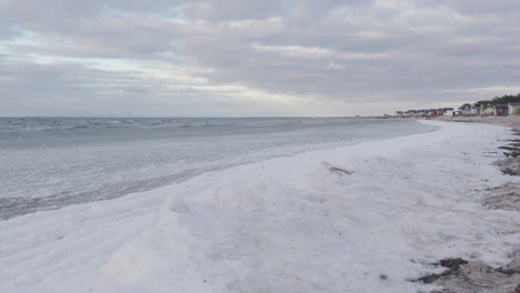 Static-shot-of-snowy-beach-and-ice-covered-sea-waves-rolling-in
