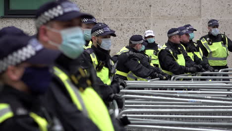 A-slow-motion-view-of-a-line-of-Metropolitan-police-officers-wearing-protective-surgical-face-masks-stand-guard-behind-metal-crowd-barriers
