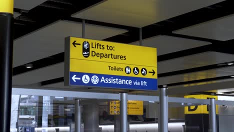 Yellow-and-blue-directional-signage-at-Heathrow-International-Airport-Terminal-3,-the-sign-provides-passengers-with-guidance-to-the-departure-terminal,-toilets-and-assisted-passenger-lift,-London,-UK