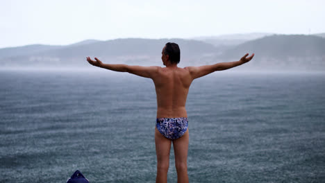 Back-View-Of-A-Man-In-Swimsuit-Standing-With-Arms-Outstretched-At-The-Beach