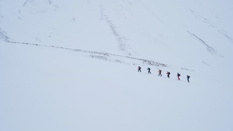 Team-of-six-hikers-climbing-snowy-winter-mountain-in-Svalbard,-handheld-view