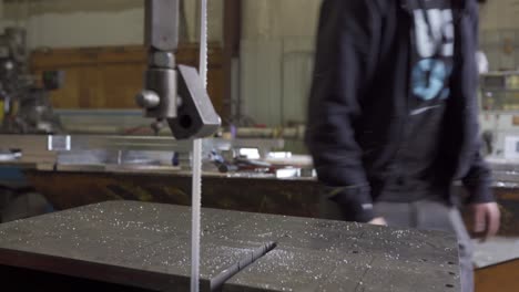 Close-Up-Of-Bandsaw-Blade-Cutting-Aluminum-With-Workman-In-Safety-Glasses-In-Background