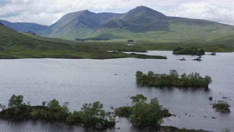 wooded-islands-on-loch-with-mountains,-Rannoch-Moor,-Highlands,-Scotland,-wide,-aerial