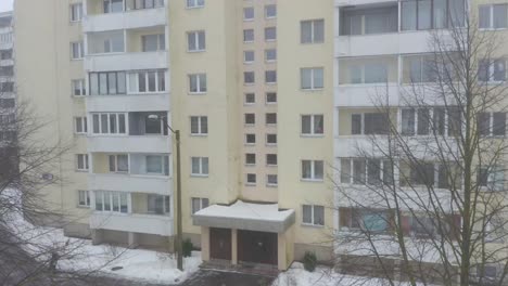 Close-drone-tilt-to-up-of-a-yellow-nine-story-Soviet-style-building-in-snowy-city