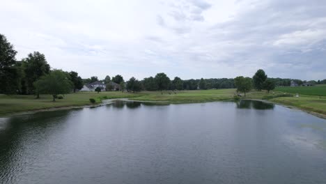 bird-fly-over-pond-on-golf-course,-drone-view