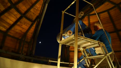 Man-using-large-telescope-in-observatory-to-look-at-moon-in-night-sky