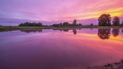 Low-angle-shot-beside-the-lake-under-colorful-sunset-sky-with-white-clouds-movement-in-timelapse