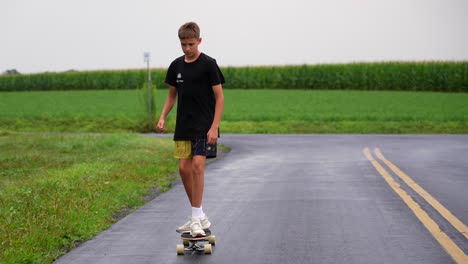 Young-white-teenage-boy-riding-skateboard-on-back-roads-in-countryside