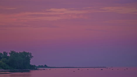 Timelapse-shot-of-purple-and-pink-sky-over-the-sea-just-after-sunset-along-the-shoreline-during-evening-time
