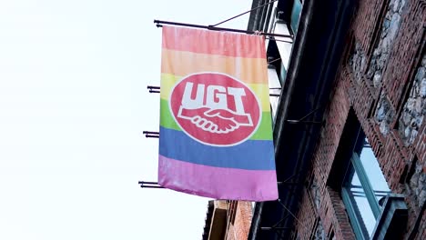 Slow-motion-of-a-waving-LGTBQ-rainbow-flag-supported-by-UGT-union-in-a-brick-building-in-Madrid,-Spain