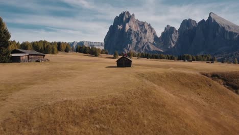 Alpe-di-Siusi-rolling-hills,-cabins-and-Dolomites-mountains-background