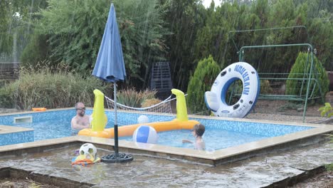 Boy-jumps-playfully-into-garden-swim-pool-in-heavy-rain-storm