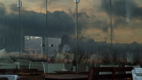 Girl-dancing-while-entering-a-sunset-club-with-cloud-reflections-on-the-window-at-Costa-da-Caparica,-Portugal