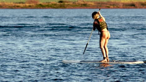 A-woman-in-a-bikini-paddleboarding-on-Lake-Paranoa-in-Brasilia,-Brazil