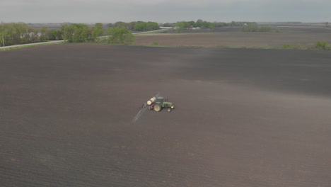Aerial-drone-shot-day-of-a-tractor-spraying-on-a-field