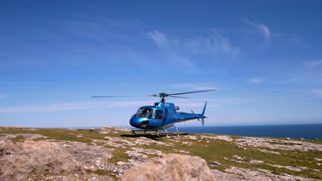 Helicóptero-Privado-Encaramado-En-La-Cima-De-Un-Acantilado-De-Montaña-Con-Vista-Al-Paisaje-Del-Océano-Azul-Con-Hélice-Girando-A-La-Derecha-Dolly
