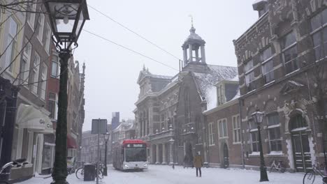 Bus-driving-through-snowy-Breestraat-road-in-Leiden-city,-Netherlands-winter