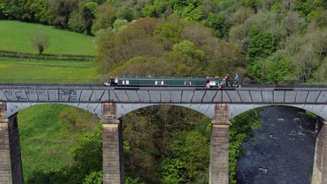 Aerial-view-following-narrow-boat-on-Trevor-basin-Pontcysyllte-aqueduct-crossing-in-Welsh-valley-countryside-static