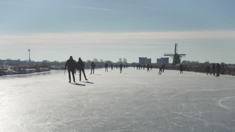 Gente-Patinando-Sobre-Hielo-En-Canales-Holandeses-Congelados-Cerca-De-Molinos-De-Viento-Tradicionales,-Invierno