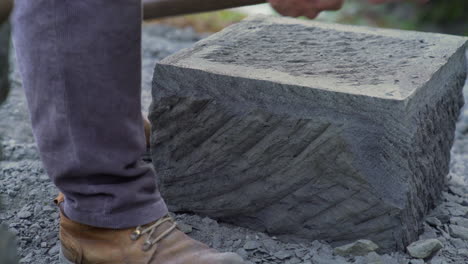 Handheld-dolly-shot-of-a-stone-craftsman-using-a-pick-to-edge-a-large-stone-brick,-in-the-city-of-Ancud,-on-the-island-of-Chiloe