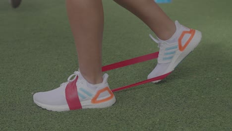 using-elastic-bands-for-exercise-with-feet-on-green-grass-and-white-tennis-shoes