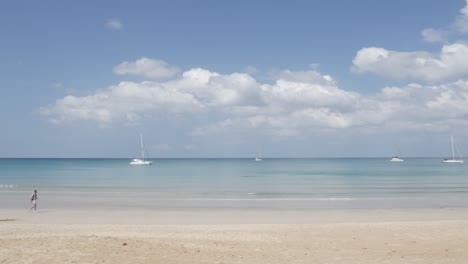 the-beach-with-a-few-yachts-in-sea,-white-sand-and-wave-from-peaceful-sea-in-sunshine-daytime