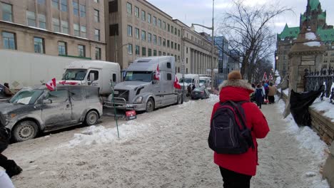 Freedom-Convoy-Supporters-With-Flags-Walking-In-The-Snowy-Sidewalk-With-Parked-Trucks-On-The-Street-At-Winter