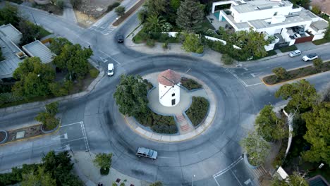 Aerial-orbit-of-Leonidas-Montes-windmill-tower-in-roundabout-with-cars-driving-surrounded-by-trees,-Lo-Barnechea,-Santiago,-Chile
