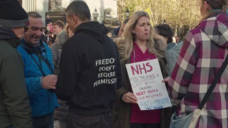 NHS-nurse-holding-placard-on-unemployment-talking-to-journalist-during-an-extinction-rebellion-protest-in-city-center-on-a-cold-winters-day-medium-shot