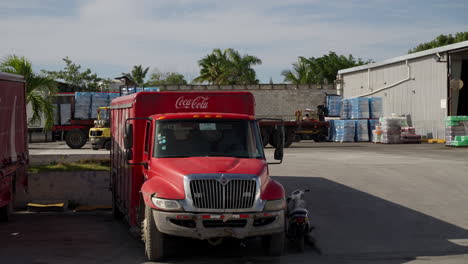Stationary-Parked-Coca-Cola-Trucks-At-Distribution-Centre-In-Punta-Cana-With-Fork-Lift-Workers-In-Background