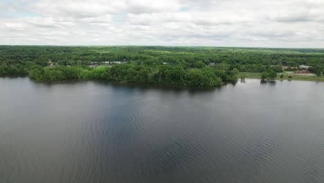 Aerial-slow-motion-view-of-lake-covered-with-forest-in-one-side,-having-a-reflection-of-sky